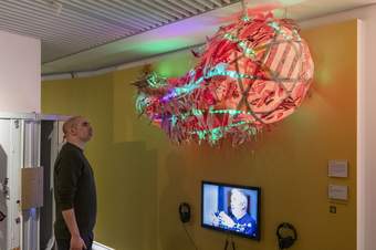 A photograph of a visitor looking up at a comet-looking artwork installation